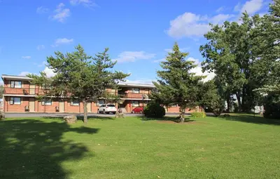 a building with trees in front of a yard at Motel Du Fleuve in Brossard