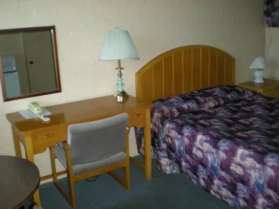 a hotel room with a desk and a bed and a bed and a table at Motel Seigneurie de Vaudreuil in Vaudreuil-Dorion