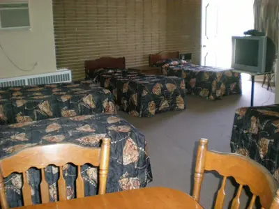 a room with two beds and a tv and chairs at Motel Seigneurie de Vaudreuil in Vaudreuil-Dorion