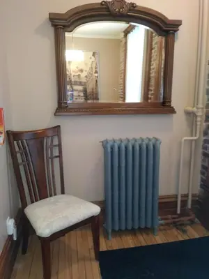 a mirror and a radiator and a chair in a room at Vieux-Old Farnham Appart-Condotel in Farnham