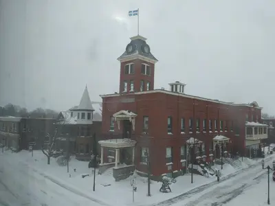 a large red brick building with a clock tower in the snow at Vieux-Old Farnham Appart-Condotel in Farnham