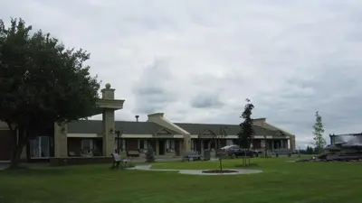 a large building with a park in front of it at Hotel Motel Le Quiet in Lac-Mégantic