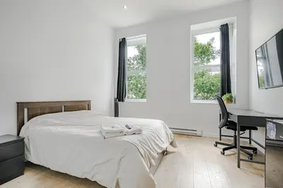 a bedroom with a bed and a desk and two windows at HoMa Homestay Hotel by Olympic Stadium Montreal Auberge-Hostel in Montréal