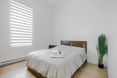 a white bedroom with a bed and a plant at HoMa Homestay Hotel by Olympic Stadium Montreal Auberge-Hostel in Montréal