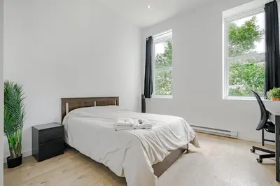 a bedroom with a bed and a desk and two windows at HoMa Homestay Hotel by Olympic Stadium Montreal Auberge-Hostel in Montréal