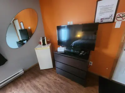 a room with a television and a dresser with a mirror at Motel Le Victo in Victoriaville