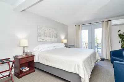 a white bedroom with a bed and a blue chair at Auberge Aux Deux Pères in Magog-Orford