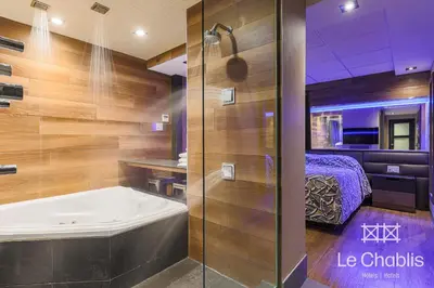 a bathroom with a bath tub and a bedroom at Hotel Le Chablis Cadillac in Montréal