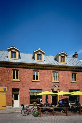 a brick building with tables and umbrellas in front of it at L'Auberge du QG in Laprairie