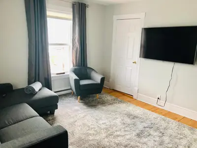 a living room with a couch and a chair and a television at Le « Lake View » de la Suite North Hatley in North Hatley