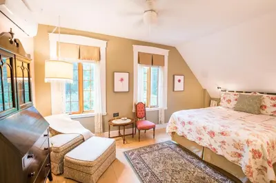 a bedroom with a bed and a chair and windows at Boisé Rivière in Bolton-Est