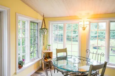 a dining room with a glass table and windows at Boisé Rivière in Bolton-Est