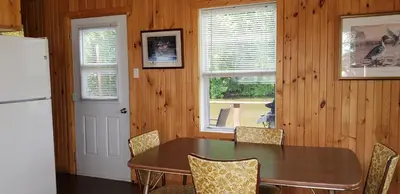 a dining room with a table and a refrigerator at Pourvoirie Stéphane Marin in Maskinongé