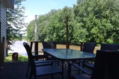a table and chairs on a deck with a view of a river at Pourvoirie Stéphane Marin in Maskinongé