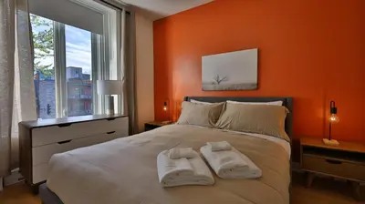 a bedroom with orange walls and a bed with two towels at Le Duplex VIP in Montréal