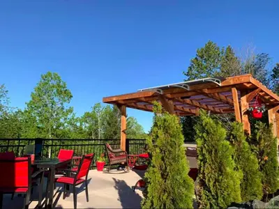 a patio with a wooden pergola and tables and chairs at La Spacieuse Riverstone CITQ3O1849 in Saint Pierre de Broughton