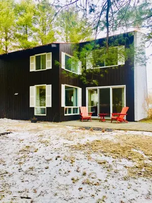 a black house with red chairs in front of it at Le Jackrabbit Orford Domaine Cheribourg in Orford