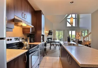 a kitchen with wooden cabinets and a dining room at Bromont-Condo sur la montagne in Bromont