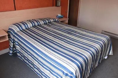 a bed with a blue and white striped blanket on it at Motel Boisé in Blainville
