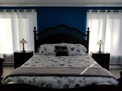 a bedroom with a large bed with blue walls and windows at Dans Les Bras de Memphré in Magog-Orford