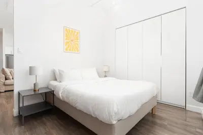 a white bedroom with a large bed and a side table at Boutique Lofts Notre Dame - Vieux Montréal in Montréal