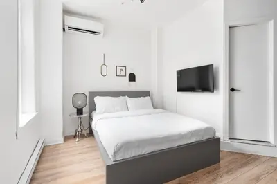 a white bedroom with a bed and a flat screen tv at Boutique Lofts Notre Dame - Vieux Montréal in Montréal