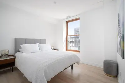 a white bedroom with a bed and a window at Le Nomade MTL in Montréal