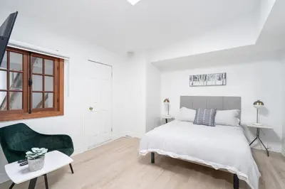 a white bedroom with a bed and a green chair at Le Nomade MTL in Montréal