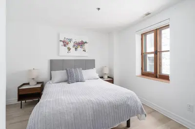a white bedroom with a bed and a window at Le Nomade MTL in Montréal