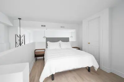 a white bedroom with a large bed with white sheets at Le Nomade MTL in Montréal