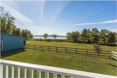 a fence on a yard with a field and water at North House - Lovely Lac-Brome 3 Bedroom Lakefront Cottage in Lac-Brome
