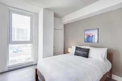 a white bedroom with a bed and a window at L'Equinox Modern Apartments by Corporate Stays in Laval