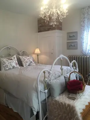 a bedroom with a white bed and a chandelier at La Belle aux Berges in Saint-Denis-sur-Richelieu