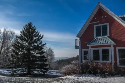 a red house with a pine tree in the snow at Auberge Le Tricorne in North Hatley
