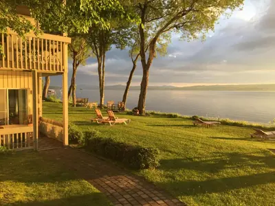 a house with chairs on the lawn next to the water at Condos Memphrémagog in Magog-Orford
