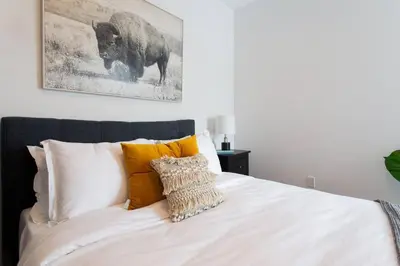 a white bed with pillows and a picture of a buffalo at Sleek Condo in the Heart of Little Italy by Den Stays in Montréal