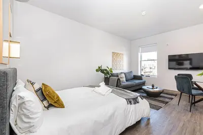 a white bedroom with a bed and a living room at New, Fresh and Luminous Studio in Le Plateau by Den Stays in Montréal