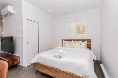 a white bedroom with a bed and a chair at Huge New Flat well Located closed on St-Denis Street by Den Stays in Montréal