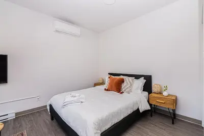 a white bedroom with a large bed with orange pillows at Wonderful New Studio close to Mount Royal By Den Stays in Montréal