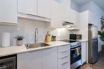 a white kitchen with a sink and a refrigerator at Wonderful New Studio close to Mount Royal By Den Stays in Montréal