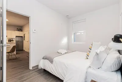 a white bedroom with a bed and a kitchen at New Urban and Well Located 1 Bedroom Apartment by Den Stays in Montréal