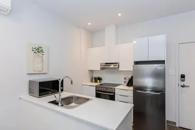 a kitchen with white cabinets and a stainless steel refrigerator at New and Perfectly Located 1 Bedroom Apartment by Den Stays in Montréal