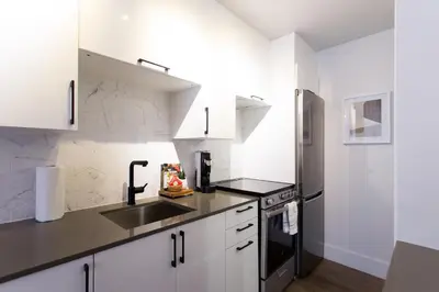 a kitchen with white cabinets and a stainless steel refrigerator at Perfect Business Trip Studio with Full Amenities by Den Stays in Montréal