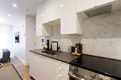 a kitchen with white cabinets and a black counter top at The Santamaria Golden Palms Studio by Den Stays in Montréal