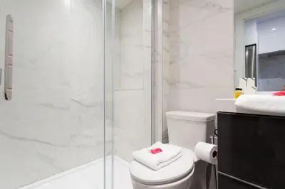 a white bathroom with a shower and a toilet at Scandinavian Studio with Full Kitchen and Bath by Den Stays in Montréal
