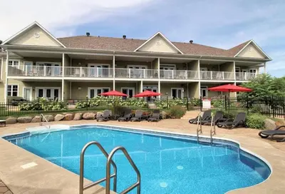 a pool in front of a hotel with chairs and umbrellas at Le Champlain Condo-Hôtel in Bromont