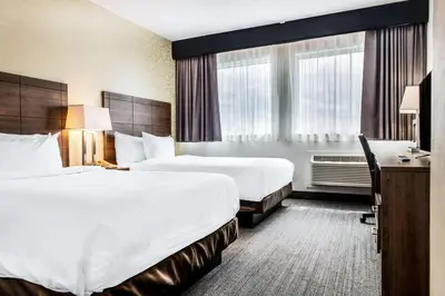 a hotel room with two beds and a desk at Quality Hotel Dorval Aeroport in Dorval