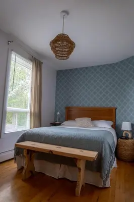 a bedroom with a bed with a wooden bench next to a window at Au coq du bonheur in Magog-Orford