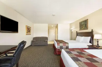 a hotel room with two beds and a chair and a television at Days Inn by Wyndham Montreal East in Montréal