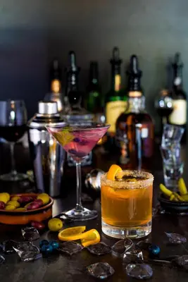two cocktails on a table with bottles of alcohol at Hôtel Château Joliette in Joliette